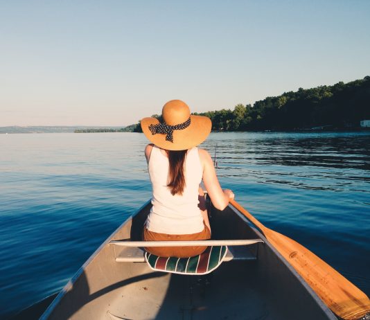 faites le plein de soleil au printemps, comme cette femme de dos dans une barque, sur un lac ensoleillé, avec un grand chapeau de paille.